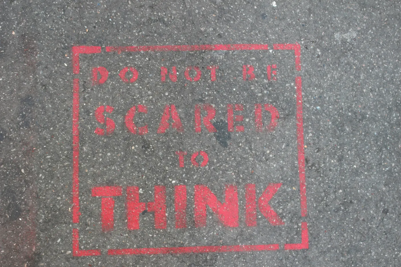 Red stencilled words on a footpath: Do not be scared to think