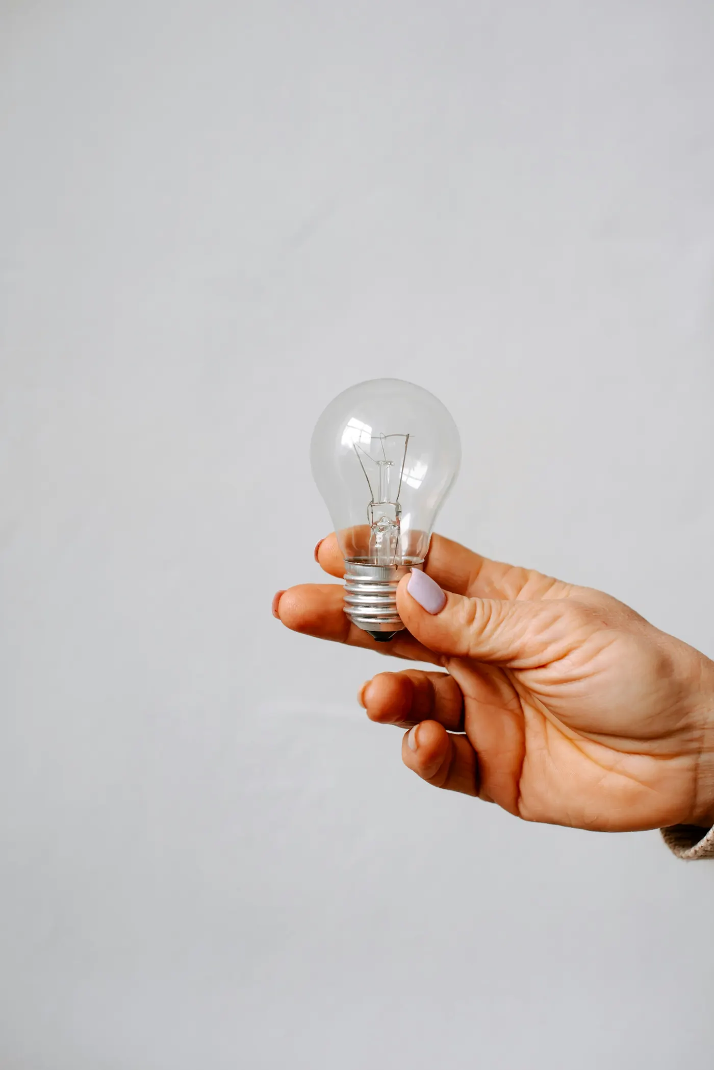 A hand holding a clear light bulb against a pale grey background
